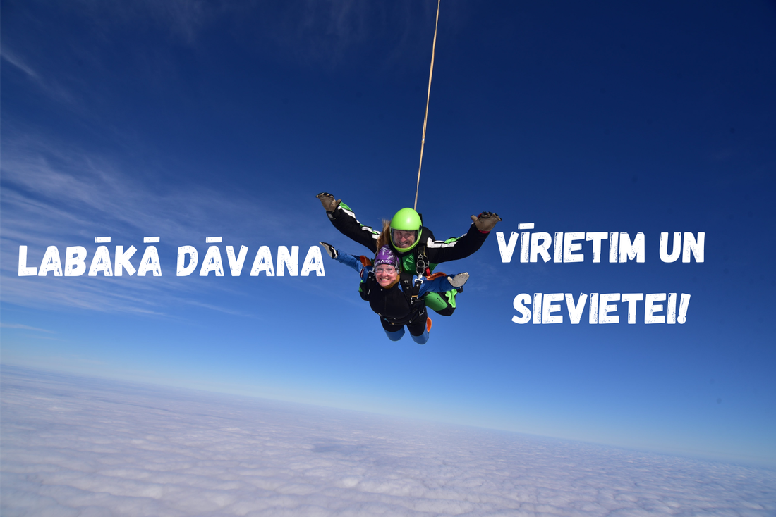 Tandēma izpletņlēciens virs mākoņiem ar skaidrām debesīm. Instruktors un pasažiere smaida brīvajā kritienā. Teksts attēlā: Labākā dāvana vīrietim un sievietei.